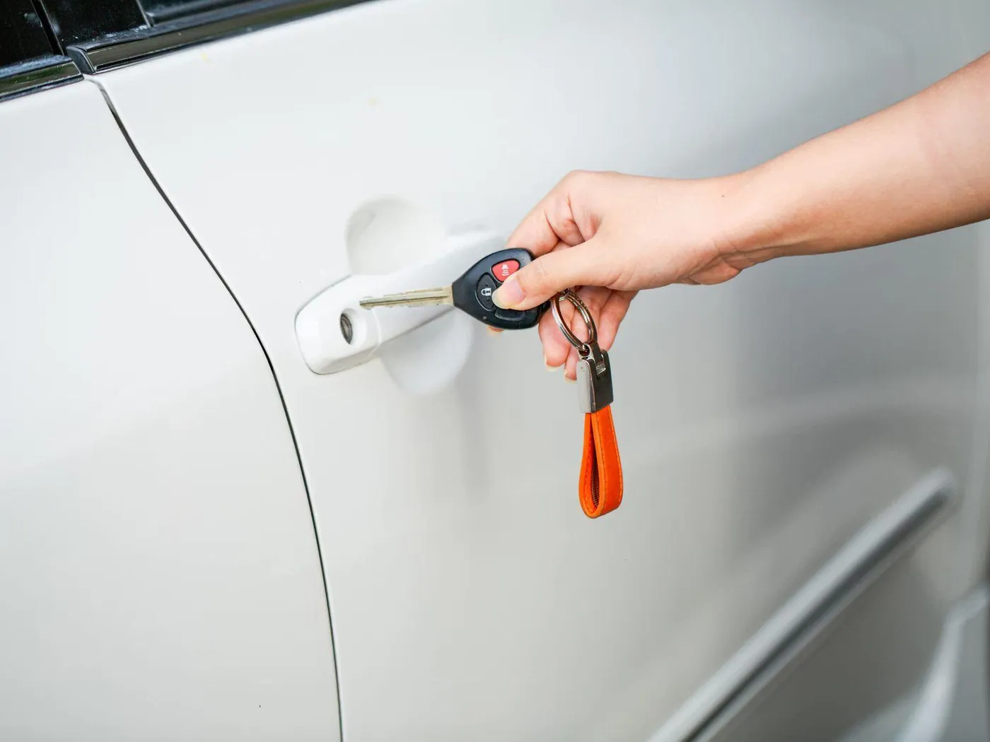 Mano abriendo la puerta de un coche blanco con su llave